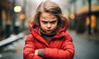 Stern-faced little girl in red winter jacket crossing arms in a defiant pose on a cold, blurred urban street background