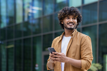 close-up portrait of a young muslim man standing outside an office center, university campus, holdin
