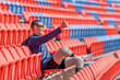 Sport man athlete prosthesis legs sit on chair of amphitheater look forward with show thumbs up in the stadium with day light.
