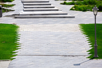 Wall Mural - pavement with stone tiles with drainage system and street light on green lawn on sunny summer park, nobody.