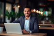 © EricMiguel - Smiling professional in suit working on laptop in a modern coffee shop.