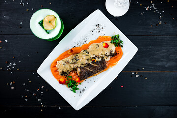 Sticker - Fried white fish with carrot puree, mushrooms in sauce, truffles and microgreens in a plate.