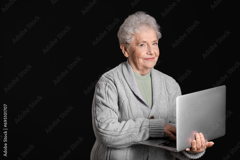 Senior woman using laptop on black background
