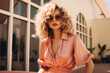 © Enigma - Fashionable woman with curly blonde hair and aviator sunglasses, dressed in a silk peach blouse, posing in an urban setting.