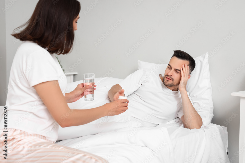 Young man taking pills from his wife in bedroom