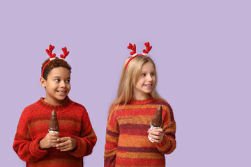 Canvas Print - Cute little children in reindeer horns with chocolate Santa Claus on lilac background