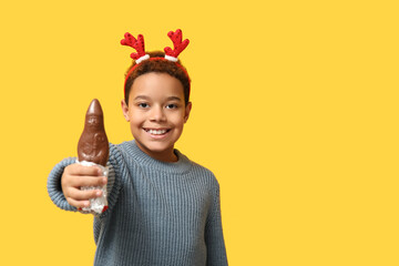 Canvas Print - Cute little African-American boy in reindeer horns with chocolate Santa Claus on yellow background