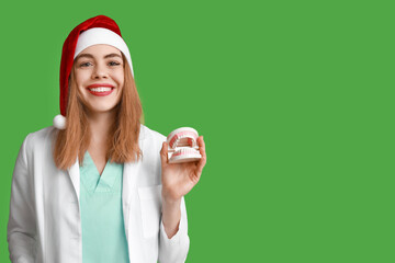 Wall Mural - Young female dentist in Santa hat with jaw model on green background