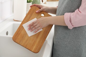 Poster - Woman wiping wooden cutting board with paper napkin at sink in kitchen, closeup