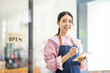 © David - Portrait of happy waitress standing at restaurant entrance. SME entrepreneur young business asian woman attend new customers near door. Smiling small business owner showing open sign in her shop.