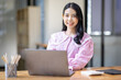 © David - Photo of cheerful joyful young asian business woman in the office working on laptop digital project sitting at desk.