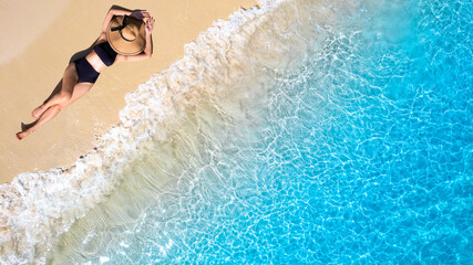 Wall Mural - Aerial view of beautiful young woman in black swimsuit lying on sandy beach near blue sea with waves at sunset Summer vacation at Andaman Island	
