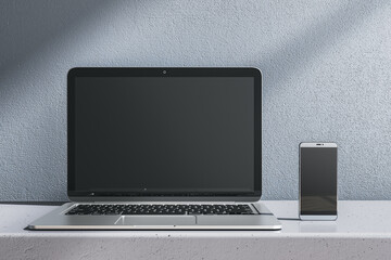 Wall Mural - Close up of empty laptop and smartphone on gray desk. Concrete wall background. Device presentation and online education concept. Mock up, 3D Rendering.