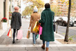 Group of female friends with colorful shopping bags strolling through city streets, enjoying the festive season's sales and winter fashion.