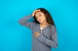Beautiful teen girl wearing blue jacket over blue background Touching forehead for illness and fever, flu and cold, virus sick.