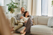 © LIGHTFIELD STUDIOS - joyful child-free couple relaxing on cozy sofa in living room and looking away, leisure in comfort