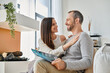 © LIGHTFIELD STUDIOS - smiling woman embracing husband reading science magazine on couch at home, child-free life