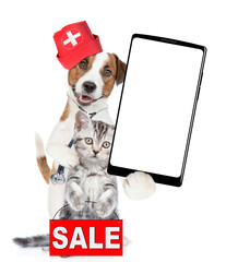 Poster - Funny jack russell terrier dressed like a doctor with stethoscope on his neck hugs tiny kitten and shows big smartphone with white blank screen in it paw. Cat shows ignboard with labeled 