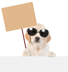 Poster - Funny Golden Retriver puppy wearing sunglasses holds empty placard above empty white banner. isolated on white background