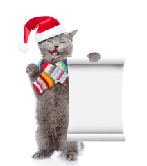 Poster - Happy kitten wearing red christmas hat and warm knitted scarf shows empty list. isolated on white background