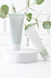 Minimalist skincare tubes on white pedestal with greenery