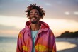 © Markus Schröder - Portrait of a grinning afro-american man in his 20s wearing a vibrant raincoat against a beautiful beach sunset. AI Generation
