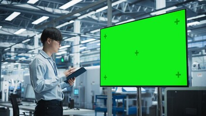 Aufkleber - Asian Male Chief Engineer Using Tablet And Looking At TV With Green Screen Chromakey On Display At Autonomous Electronics Factory With Robotic Arms. Man Overlooking Assembly Of New Devices In Office.