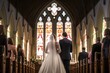  a bride and groom walking down the aisle of a church with stained glass windows and pews on either side of the aisle and a man and woman at the back of the aisle.
