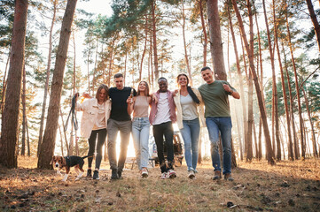 Full height photo, standing with dog. Group of friends are together in the forest