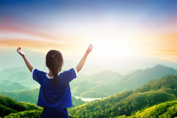 A kid standing on the top of the mountain and raise  hands to worship god.