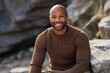 Portrait of a grinning man in his 30s dressed in a warm wool sweater against a rocky cliff background. AI Generation