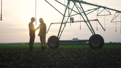 Poster - irrigation agriculture. two silhouette farmers working in the field examining installation for irrigating corn in field. irrigation agriculture concept. farmers work business in a field with corn