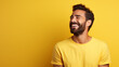 © PhotoFlex - Handsome man with beard wearing casual yellow tshirt over yellow background looking away to side with smile on face, natural expression. laughing confident.