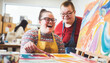 © PhotoGranary - Adult students with Down syndrome enjoying an art class, creating vibrant paintings with laughter.