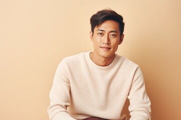 Canvas Print - Portrait of a content asian man in his 20s dressed in a warm wool sweater against a pastel or soft colors background. AI Generation