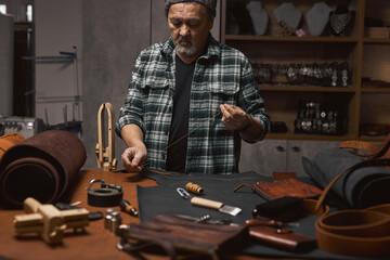 Wall Mural - handsome bearded tailor prepares thread and needle for sewing, portrait of talented craftsman working at workshop