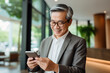 Portrait of an age-old happy Asian man with glasses and a phone in the office