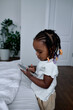 nice pritty toddler with dreads playing games on smart phone, standing in the bedroom, close up side vieew shot. kid touching the scree, watches video, make video, phone call