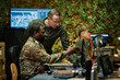 © Seventyfour - Young African American military officer in camouflage uniform pointing at computer screen while explaining graphic data to colleague