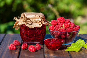 Wall Mural - Red raspberry jam and fresh raspberry on a rustic wooden table outdoors near garden. Rustic style, closeup