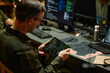 © Seventyfour - Young male military officer looking at screen of tablet in his hands while sitting by workplace in front of computer monitors