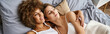 young lesbian and multiethnic couple in pajamas lying together on bed at home, lgbtq love banner