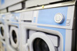 © pressmaster - Part of new white washing machine with switching knob on blue panel standing next to group of other items in modern laundry