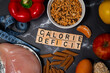 Flat lay photo showing calorie deficit. The inscription calorie deficit next to fruit, vegetables, meat and pasta. A healthy, tasty and balanced diet