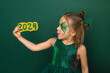 A funny girl with a drawing on her face in the shape of a dragon looks at the numbers of the 2024 new year with surprise