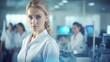 © Dirk - copy space, stockphoto, young woman scientist with white labcoat and a modern Medical Laboratory with Team of labtechnicians in the background. International Day of Women and Girls in Science.