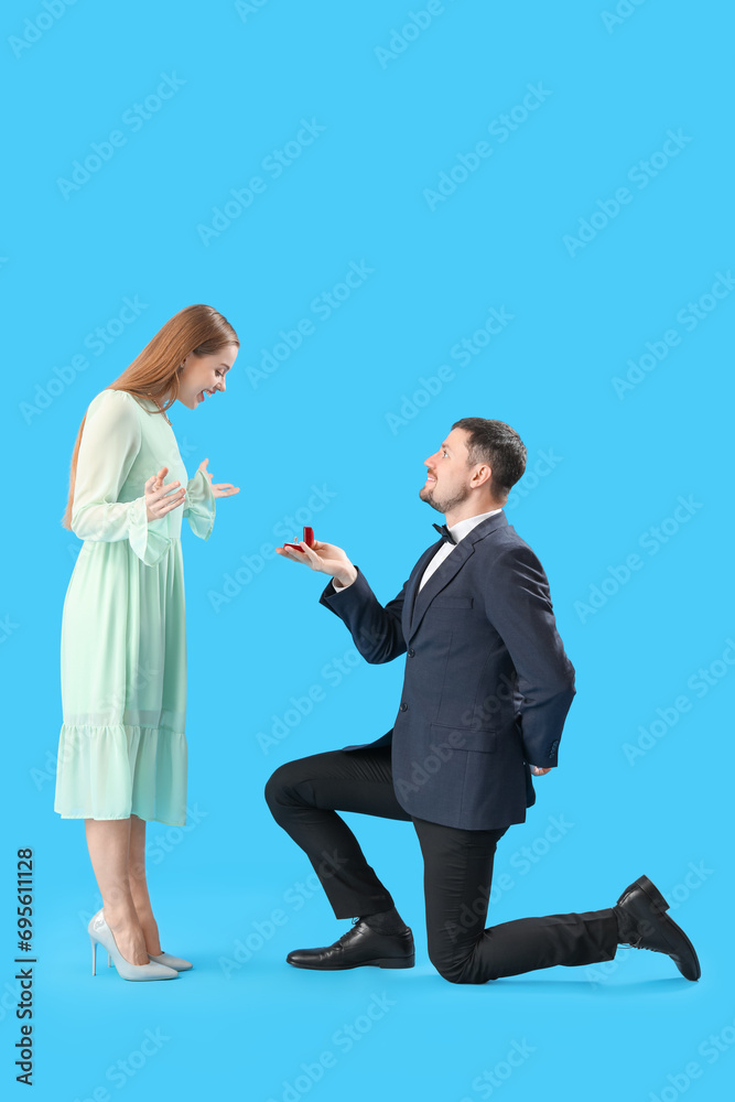 Young man in suit proposing to his girlfriend on blue background