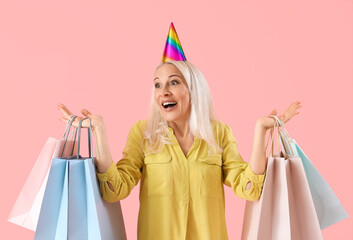 Poster - Mature woman with bags of birthday gifts on pink background