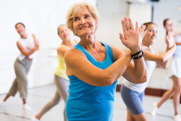 Portrait of smiling mature woman practicing ballet dance moves during group class in choreographic studio