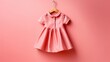 Pink dress for little girl on wooden hanger on pink background